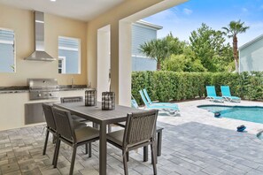 Eine Außenpatio mit Esstisch, Stühlen, Grill und Poolbereich mit Liegestühlen.