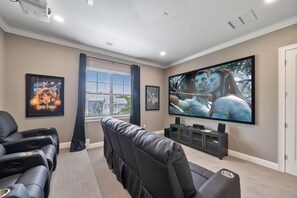 Une salle de cinéma privée équipée d’un grand téléviseur à écran plat, de fauteuils inclinables et de reproductions d’affiches de films encadrées.