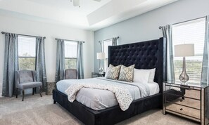 A bedroom with a large bed, a chair, a bedside table, and a window with curtains. - Stylish Villa With Unreal Themed Bedroom at Reunion (Kissimmee)
