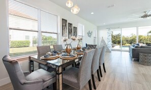 A dining area with a glass table, grey upholstered chairs, and decorative items. - Stylish Villa With Unreal Themed Bedroom at Reunion (Kissimmee)