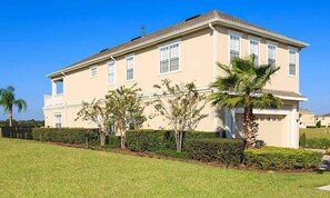 A two-story building with a beige facade, multiple windows, and a well-maintained lawn with small trees and a palm tree. - Lively Home With Water Views at Reunion (Kissimmee)