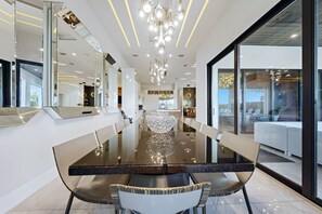 Un espace de salle à manger moderne avec une table en verre, des chaises blanches et un lustre.