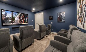 Una sala de cinema amb un televisor de pantalla plana gran, butaques reclinables grises i una porta.
