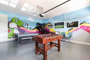 Een kamer met een tafelvoetbaltafel, een beamer en een kleurrijke muurschildering.