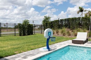 Una piscina amb un aro de bàsquet, una cadira de relax i un pati tancat per una tanca.