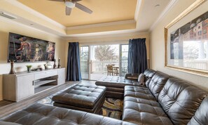 A spacious living room with a large sectional sofa, a flat-screen TV mounted on the wall, and a ceiling fan. - Spacious Elegant Condo With Private Balcony at Reunion (Kissimmee)