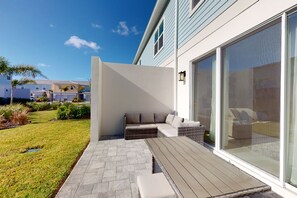 A modern outdoor patio with a wooden deck, a built-in seating area, and a large sliding glass door. - Voguish Townhouse With Games Room at Encore (Kissimmee)