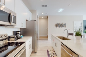 A modern kitchen with stainless steel appliances, a built-in microwave, a coffee maker, and a sink. - Voguish Townhouse With Games Room at Encore (Kissimmee)