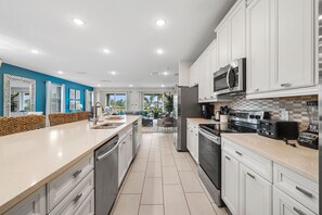 A modern kitchen with white cabinetry, stainless steel appliances, and a large island with a sink. - Homely Villa With Games Room at Encore (Kissimmee)