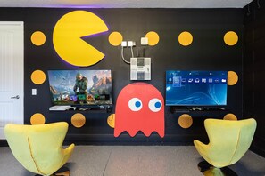Ein Spielzimmer mit zwei großen Monitoren, einer Pac-Man-Dekoration und zwei gelben Stühlen.