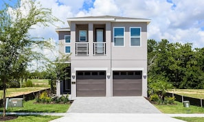 A two-story modern house with a garage, surrounded by greenery and a clear sky. - Stylish Home With Themed Bedroom at Reunion (Kissimmee)