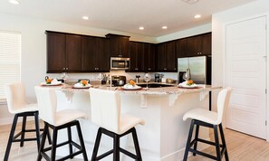 A modern kitchen with dark wood cabinets, a central island with bar stools, and stainless steel appliances. - Stylish Home With Themed Bedroom at Reunion (Kissimmee)