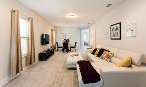 A living room with a white sofa, a TV, a dining table with chairs, and a fireplace. - Stylish Home With Themed Bedroom at Reunion (Kissimmee)