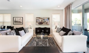 A modern living room with two white sofas, a glass coffee table, and a black entertainment unit. - Stylish Home With Themed Bedroom at Reunion (Kissimmee)