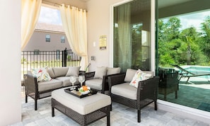 A sunlit patio with wicker furniture, a glass door leading to a pool, and a view of a house in the background. - Stylish Home With Themed Bedroom at Reunion (Kissimmee)