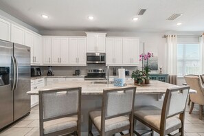 Une cuisine moderne avec des meubles blancs, des appareils en acier inoxydable et un îlot central doté de chaises.