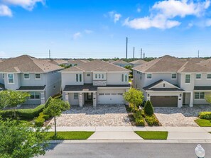 A residential area with multiple two-story houses featuring front garages, paved driveways, and well-maintained lawns. - The Cheerful Cinematic Haven at Encore Resort (Kissimmee)