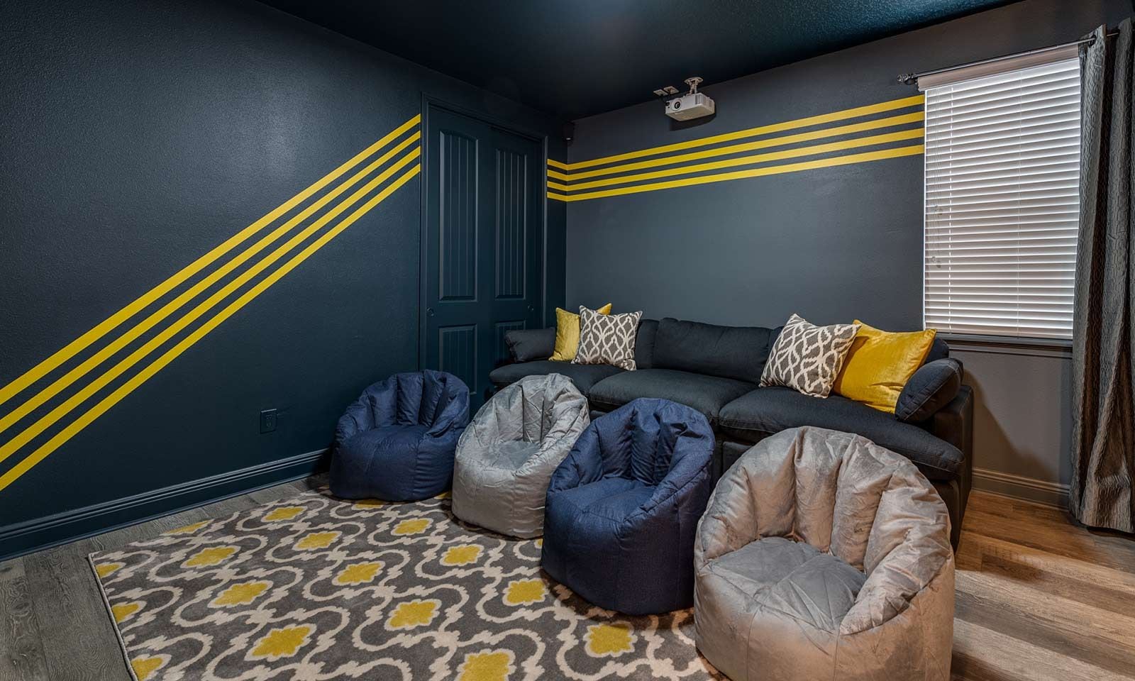 A room with a dark blue wall, yellow stripes, a sofa with patterned cushions, and three bean bags.