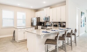 A modern kitchen with white cabinets, granite countertops, stainless steel appliances, and a central island with bar stools. - Marvelous Villa With Galactic Themed Bedroom at Encore (Kissimmee)