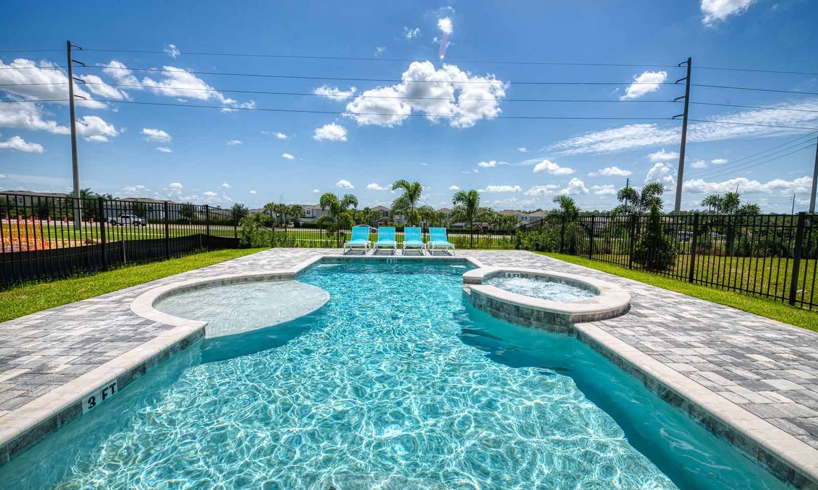 A swimming pool with a hot tub, surrounded by a fence and palm trees.