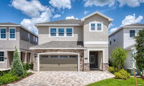 A two-story house with a garage, stone foundation, and a well-maintained lawn. - Marvelous Villa With Galactic Themed Bedroom at Encore (Kissimmee)