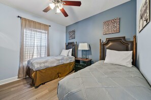 Ein Schlafzimmer mit zwei Betten, einem Deckenventilator, einem Fenster mit Vorhängen und Bildern an den Wänden.