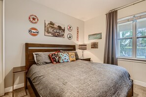 Ein Schlafzimmer mit einem Bett, Kissen, einem Nachttisch, einer Lampe und Wanddekorationen, darunter alte Autoembleme und ein Chevrolet-Schild.