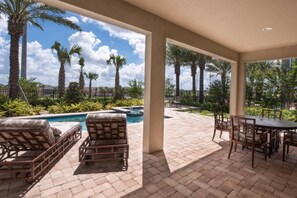 A covered outdoor area with a pool, lounge chairs, and a table. - Encore Villa: Pool, Spa, Minutes to Disney (Kissimmee)