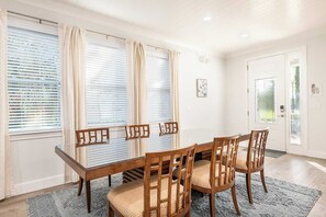 A dining area with a wooden table and chairs, large windows with blinds, and a door with a glass panel. - Encore Villa: Pool, Spa, Minutes to Disney (Kissimmee)