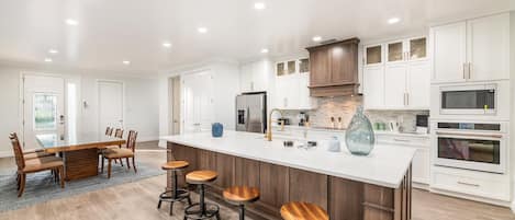 A modern kitchen with white cabinetry, a central island with stools, and built-in appliances.
