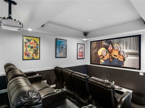 A home theater room with black leather reclining seats, a large flat-screen TV, and framed posters on the wall. - Ultra-modern Villa On Golf Course at Reunion (Kissimmee)