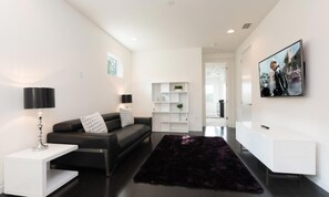 A modern living room with a black leather sofa, white side tables, a black rug, and a white entertainment unit with a mounted TV. - Ultra-modern Villa On Golf Course at Reunion (Kissimmee)