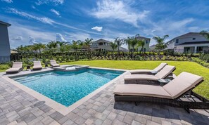 A rectangular swimming pool with lounge chairs and a small waterfall feature. - Stylish Home With Galactic Themed Bedroom at Encore (Kissimmee)