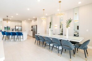 A modern kitchen with a central island, bar seating, and a dining area with chairs. - Grand Villa With Games Room at Encore (Kissimmee)