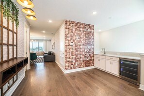 A modern kitchen with a brick-patterned accent wall, wooden flooring, and built-in appliances. - Grand Villa With Games Room at Encore (Kissimmee)