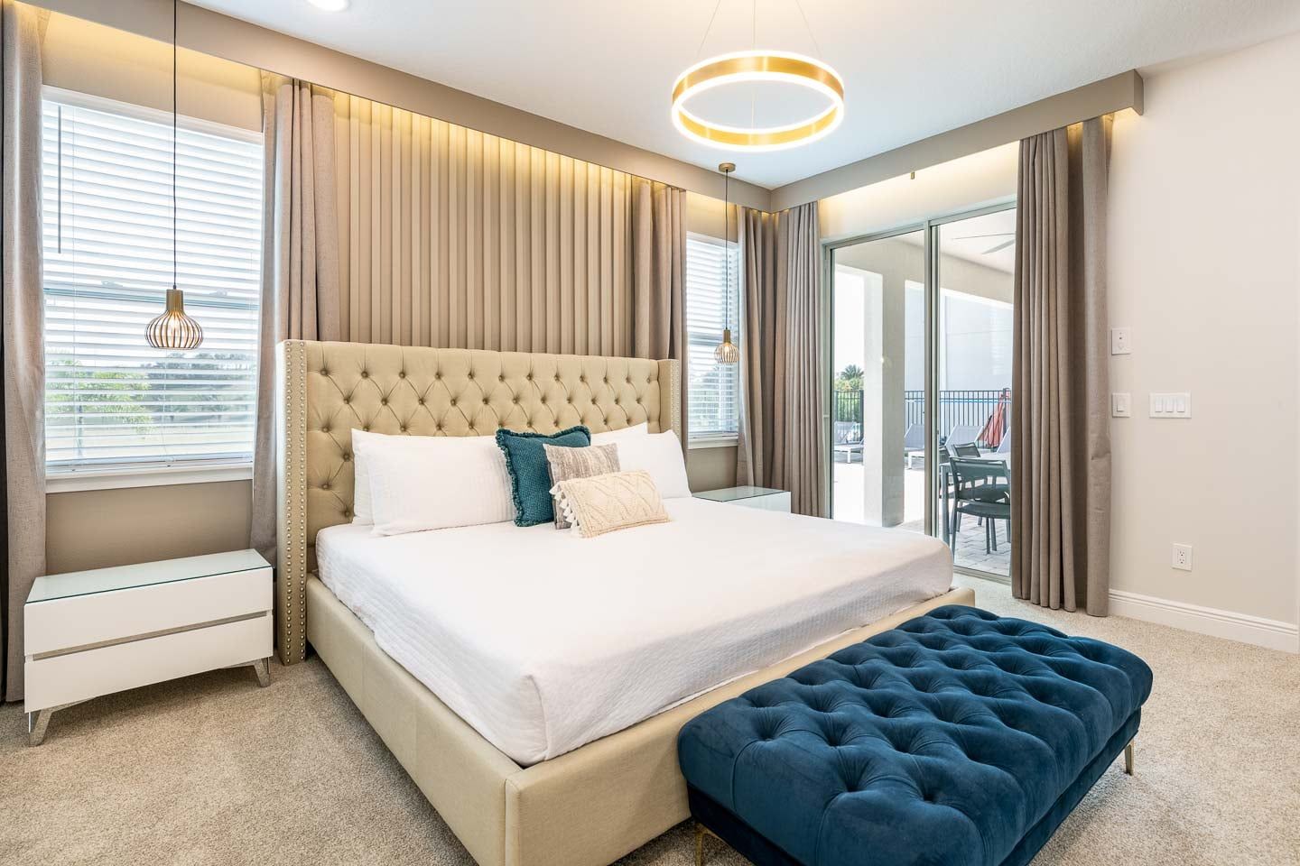 Quarto com uma cama grande, mesa de cabeceira, um banco, luminária pendente e vista através de uma porta de vidro.