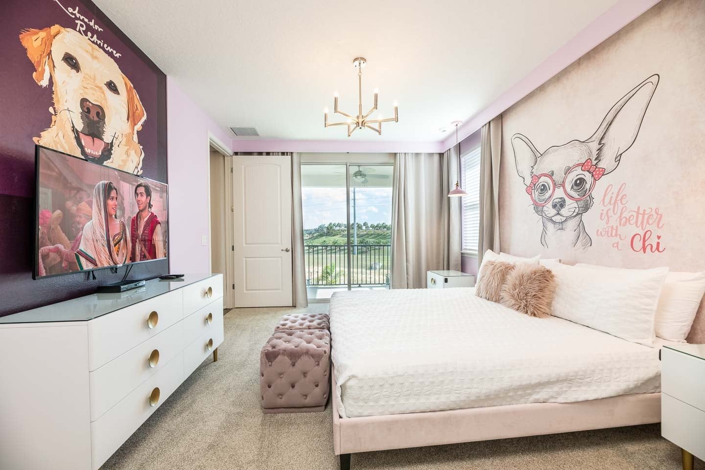 A bedroom with a large bed, a television, a chandelier, and a balcony with a view.