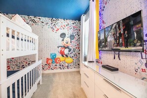 A child's room with a Mickey Mouse mural, a crib, a TV, and a wall with musical notes and symbols. - Grand Villa With Games Room at Encore (Kissimmee)