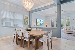 A dining area with a wooden table and chairs, a chandelier, and artwork on the walls. - Modern Seaside Cottage w Private Pool & Game Room (Kissimmee)