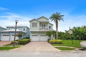 A two-story house with a front porch, a garage, and a palm tree. - Modern Seaside Cottage w Private Pool & Game Room (Kissimmee)