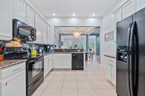A modern kitchen with white cabinetry, a black refrigerator, and a central island with a sink. - Modern Seaside Cottage w Private Pool & Game Room (Kissimmee)