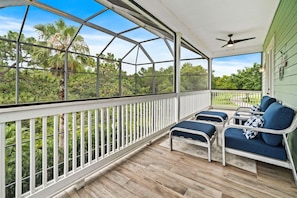 A covered porch with a view of trees, a ceiling fan, and outdoor furniture. - Modern Seaside Cottage w Private Pool & Game Room (Kissimmee)