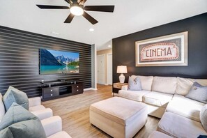 Un salon moderne doté d’un téléviseur à écran plat, d’un ventilateur de plafond, d’un canapé et d’une enseigne murale sur laquelle on peut lire le mot « CINÉMA ».