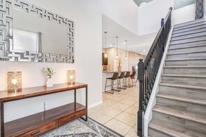 A modern interior with a wooden staircase, a console table, and a patterned rug. - Orlando 6BR Villa With Private Pool at Windsor Westside (Kissimmee)