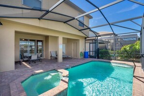Un espace piscine doté d’une structure en verre, une terrasse avec des chaises et une porte donnant accès à un espace intérieur.