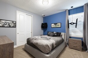Ein Schlafzimmer mit einem Bett, einem Schminktisch, einer Tür und einem fenster mit Vorhängen.