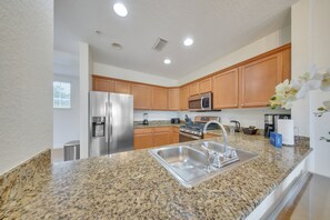 A modern kitchen with granite countertops, stainless steel appliances, wooden cabinets, and a built-in microwave. - The Golf Vista Townhome at Reunion (Kissimmee)