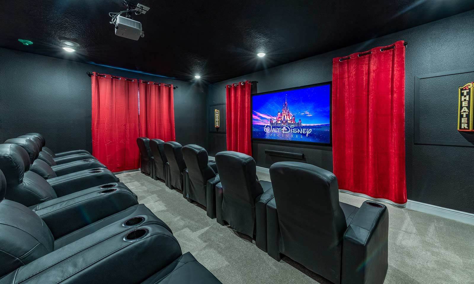 Ein Theaterraum mit schwarzen Ledersesseln, roten Vorhängen und einer großen Leinwand, die einen Film zeigt.