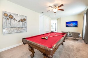 A pool table in a room with a ceiling fan, a painting, a television, and a door leading to another room. - Encore Villa: Pool & Spa, 4 Blocks to Waterpark (Kissimmee)
