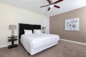 A bedroom with a large bed, a ceiling fan, a nightstand with a lamp, and a wall-mounted artwork. - Encore Villa: Pool & Spa, 4 Blocks to Waterpark (Kissimmee)